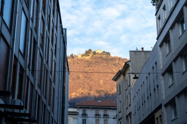 Arka planda dağ olan bir şehir sokağı. Binalar yüksek ve gökyüzü mavi.