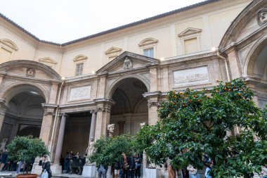 Ortasında avlu olan büyük bir bina. İnsanlar dikilip ağaçlara bakıyor.