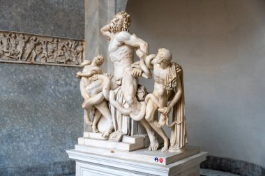 Üç adam ve bir yılanın heykeli. Heykel beyaz ve bir kaide üzerinde.