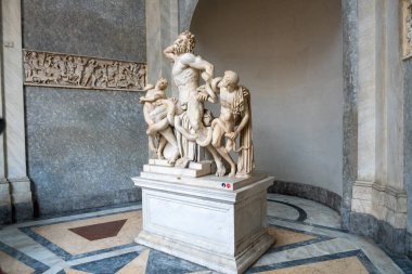 Bir erkek ve iki kadın heykeli bir kaidede oturuyor. Heykel beyazdır ve ihtişamlı ve önemlidir. Sahne mermer zemin ve heykelin arkasında duvar olan bir odada geçiyor.