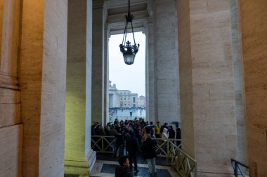 Büyük bir kalabalık büyük bir açık alanda toplanıyor, muhtemelen bir katedral ya da büyük bir bina. Atmosfer hareketli ve hareketli, her yaştan insan aylak aylak dolaşıp sosyalleşiyor.
