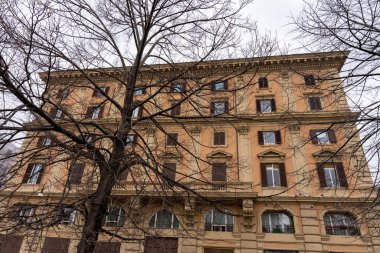 Önünde ağaç olan büyük bir bina. Bina kahverengi ve bir sürü penceresi var.