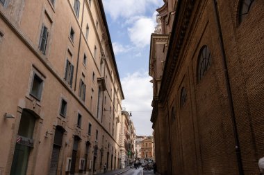Sağında tuğla bina olan dar bir cadde. Sokaklar boş ve gökyüzü bulutlu.
