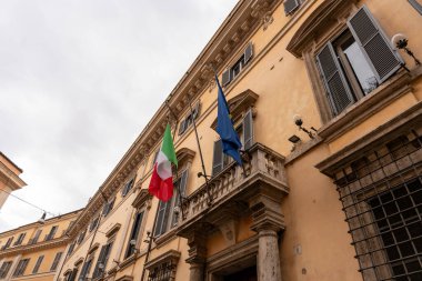 Balkonunda mavi bayrak olan bir bina. Bina sarı ve balkonunda kırmızı ve beyaz bir bayrak var.