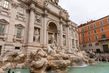 Önünde çeşme olan büyük bir bina. Çeşme taşlarla çevrili ve insan ve hayvan heykelleri var. Bina eski ve çok detay içeriyor.
