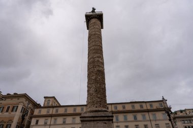 Üzerinde heykel olan uzun bir kolon. Gökyüzü bulutlu ve bina eski.