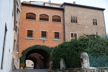 Önünde yeşil çalılar olan tuğla bir bina. Binanın bir sürü penceresi ve geniş bir kemer yolu var.