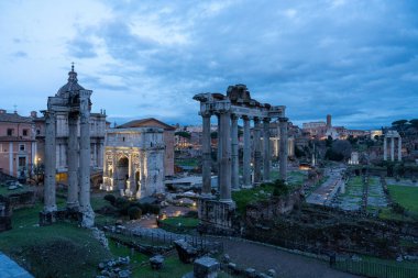 Geceleri büyük, antik bir Roma şehri. Binalar ışıklarla aydınlatılıyor, gizem ve entrika hissi yaratıyor. Bulutlu gökyüzü karamsar atmosfere ekleniyor