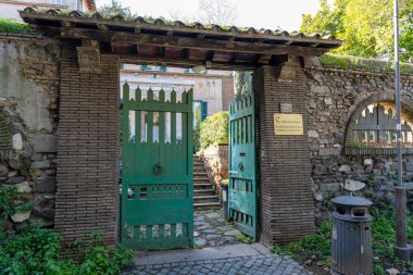 Bir binanın girişi bir avluya açıktır. Kapı yeşil ve avlu taş bir duvarla çevrili.