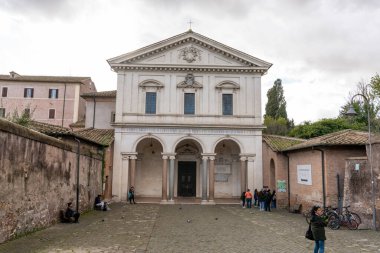 Geniş kemerli, yanında tabela olan büyük beyaz bir bina. İnsanlar binanın dışında bekliyor.