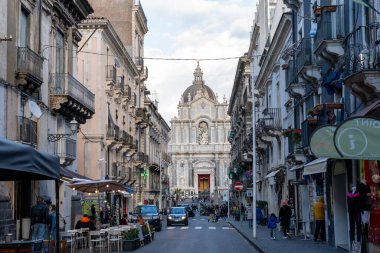 Arka planda büyük bir kilise olan işlek bir cadde. Cadde dükkan ve restoranlarla dolu ve etrafta bir sürü insan dolaşıyor. Atmosfer hareketli ve hareketli, arabalarla.