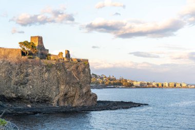 Okyanusa ve kasabaya bakan kayalık bir uçurum. Gökyüzü bulutlu ve güneş batıyor.