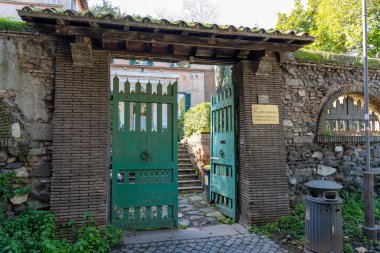 Bir binanın girişi bir avluya açıktır. Kapı yeşil ve avlu taş bir duvarla çevrili.