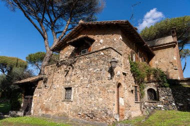 Bir sürü penceresi ve balkonu olan büyük bir taş bina. Bina ağaçlarla çevrili ve bir sürü yeşilliği var.