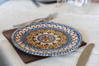 Masadaki bir peçetenin üzerinde mavi ve beyaz desenli bir tabak duruyor. Masa takımı çatal ve bıçakla tamamlandı.