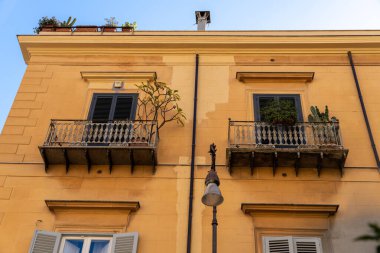 Balkonları ve bitkileri olan iki sarı bina. Binalar eski ve kırsal bir havası var.