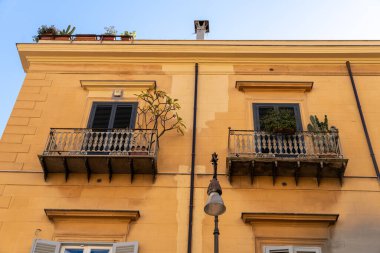 Balkonları ve bitkileri olan iki sarı bina. Binalar eski ve kırsal bir havası var.