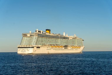 Büyük bir yolcu gemisi okyanusta yelken açıyor. Gemi beyaz ve sarıdır ve sudaki en büyük gemidir. Gökyüzü açık ve mavidir ve güneş ışıl ışıl parlar.