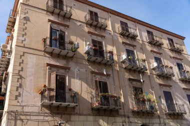 Balkonları ve saksı bitkileri olan büyük bir bina. Bina kahverengi ve bir sürü penceresi var.