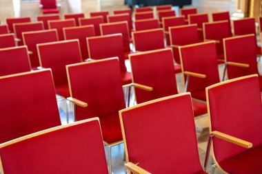 Büyük bir odada bir sıra kırmızı sandalye boş. Sandalyeler sıra sıra dizilmiş, bazı sandalyeler odanın ön tarafına bakıyor ve diğerleri de diğer tarafa bakıyor.
