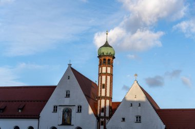 Tepesinde yeşil kubbe olan yüksek bir bina. Bina beyaz ve kırmızı bir çatısı var. Gökyüzü mavi ve bazı bulutlar var.