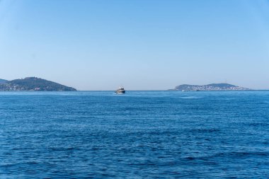 Arka planda açık mavi gökyüzü olan bir tekne okyanusta yüzüyor. Gökyüzü çok aydınlık ve su sakin.