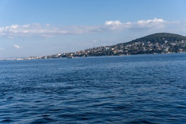 Arka planda dağ olan sakin mavi bir okyanus. Su durgun ve gökyüzü berrak.