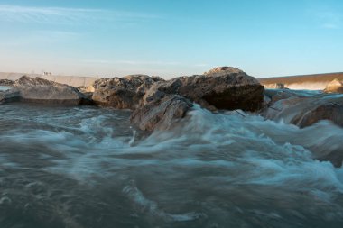 Su kayaların arasında akıyor, huzurlu ve sakin bir atmosfer yaratıyor. Kayalar sahnenin her tarafına dağılmış, bazıları suya daha yakın, bazıları ise daha uzaklarda.