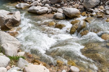 Büyük kayalar arasında bir su akıntısı akar. Sahne huzurlu ve sakin, su kayaların üzerinden geçerken sakinleştirici bir ses çıkarıyor.