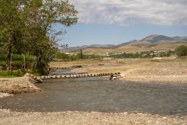 Ahşap köprüsü olan bir nehir. Köprü kütüklerden yapılmıştır ve nehrin ortasındadır. Su sakin ve gökyüzü berrak.