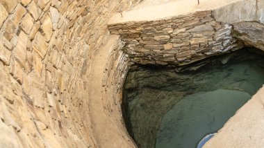 Ortasında küçük bir su havuzu olan taş bir duvar. Havuz taşlarla çevrili ve kenarında taş bir duvar var.