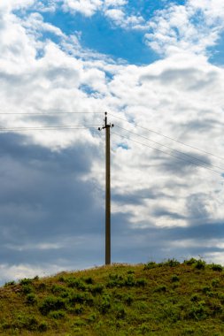 Üzerinde kablolar olan uzun bir direk bir tarlada duruyor. Gökyüzü bulutlu ve güneş görünmüyor.