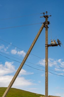 Üzerinde kablolar olan uzun bir direk gökyüzünde. Gökyüzü mavi ve bazı bulutlar var.