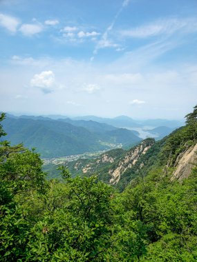 İçinden nehir akan bir dağ sırası. Gökyüzü açık ve mavi. Ağaçlar yemyeşil.