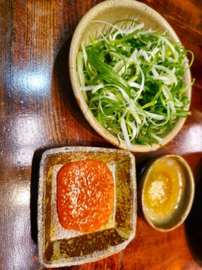 İçinde kırmızı sos olan üç kase yiyecek olan bir masa. Diğer iki kasede yeşil sebze var.