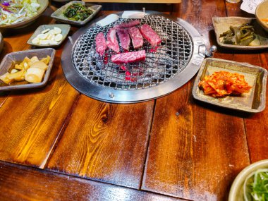 Izgara ve üzerinde et, sebze ve kimchi içeren çeşitli yiyecekler olan bir masa.