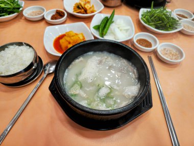 Bir kase çorba diğer kase ve kaşıklarla bir masada oturur. Çorba beyaz ve içinde yeşil bir sebze var. Masa yemek çubukları ve kaşıkla hazırlandı.