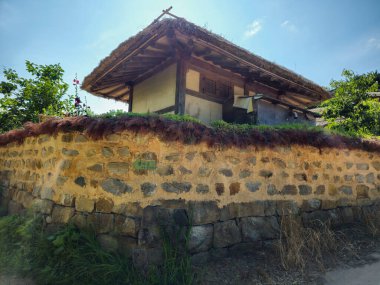 Üzerinde çatı olan taştan bir duvar. Çatı samandan yapılmıştır. Duvar kahverengi ve üzerinde bir sürü yosun var.