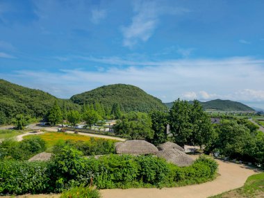 Köye giden toprak yolu olan yemyeşil bir yamaç. Gökyüzü açık ve mavi, ağaçlar dolu ve yeşil