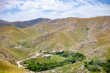 Vadide küçük bir köyü olan bir dağ sırası. Köy ağaçlarla çevrilidir ve dağlar otlarla kaplıdır. Gökyüzü açık ve güneş parlıyor.