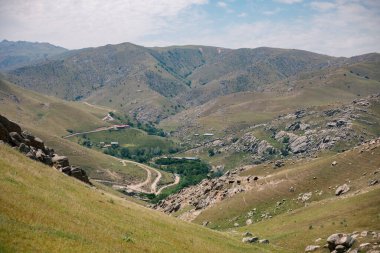 Aralarında vadi olan bir dağ sırası. Vadi evler ve bir yol ile dolu. Dağlar çimen ve kayalarla kaplıdır.