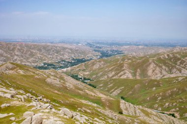 Üzerinde açık mavi gökyüzü olan güzel bir dağ sırası. Dağlar yemyeşil çimlerle kaplıdır ve sahnenin her tarafına dağılmış birkaç küçük tepe vardır.