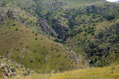 Ortasında vadi olan bir dağ sırası. Vadi yeşildir ve birkaç ağacı vardır.