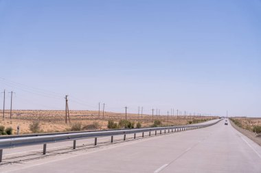 Uzun, boş bir yolda bir araba sürüyordu. Gökyüzü açık ve mavi. Yol elektrik hatlarıyla dolu ve yolda başka araba yok.