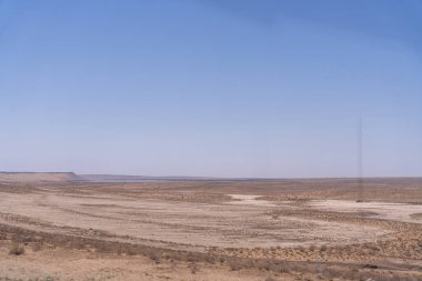 Arka planda mavi gökyüzü olan bir çöl manzarası. Gökyüzü açık ve güneş parlıyor.