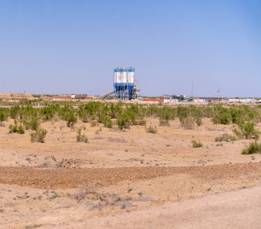 Uzakta büyük bir çimento yapısı olan bir çöl manzarası. Gökyüzü açık ve mavidir, ve güneş parlıyor. Boşluk ve yalnızlık kavramı, uçsuz bucaksız kumla