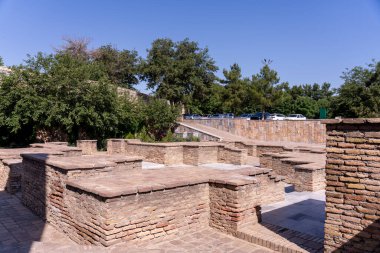 Taş duvarlı ve birkaç banklı bir avlu. Avlu ağaçlarla çevrili.