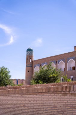 Tepesinde mavi kubbe olan yüksek bir bina. Bina tuğla bir duvarla çevrili. Gökyüzü açık ve mavi