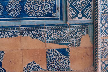 Duvardaki mavi ve beyaz fayansların çiçek desenleri var. Duvar taştan yapılmış ve pürüzlü bir dokusu var.