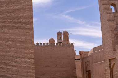 Tepesinde kule olan tuğla bir bina. Kule bir duvarla çevrilidir. Gökyüzü mavi ve bulutlar var